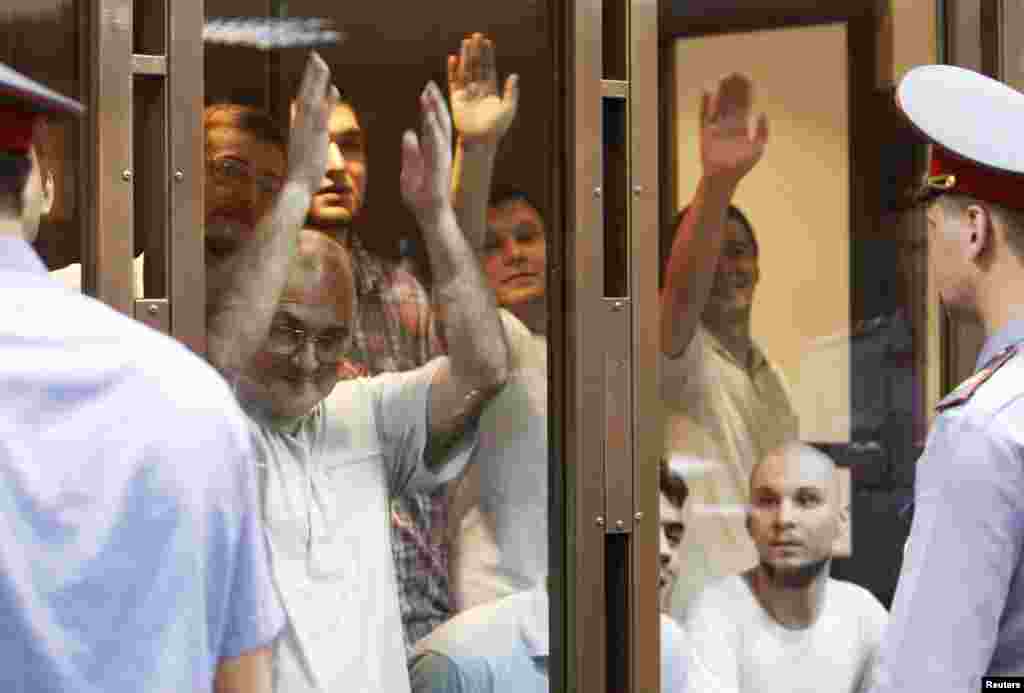 Defendants facing trial over clashes with police during an anti-Putin protest last year gesture inside a glass-walled cage before a court hearing in Moscow. (Reuters/Sergei Karpukhin)