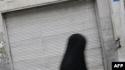 An Iranian woman walks past a closed shop in Tehran. The state of the country's economy is seen as the critical issue in the June 12 presidential election.