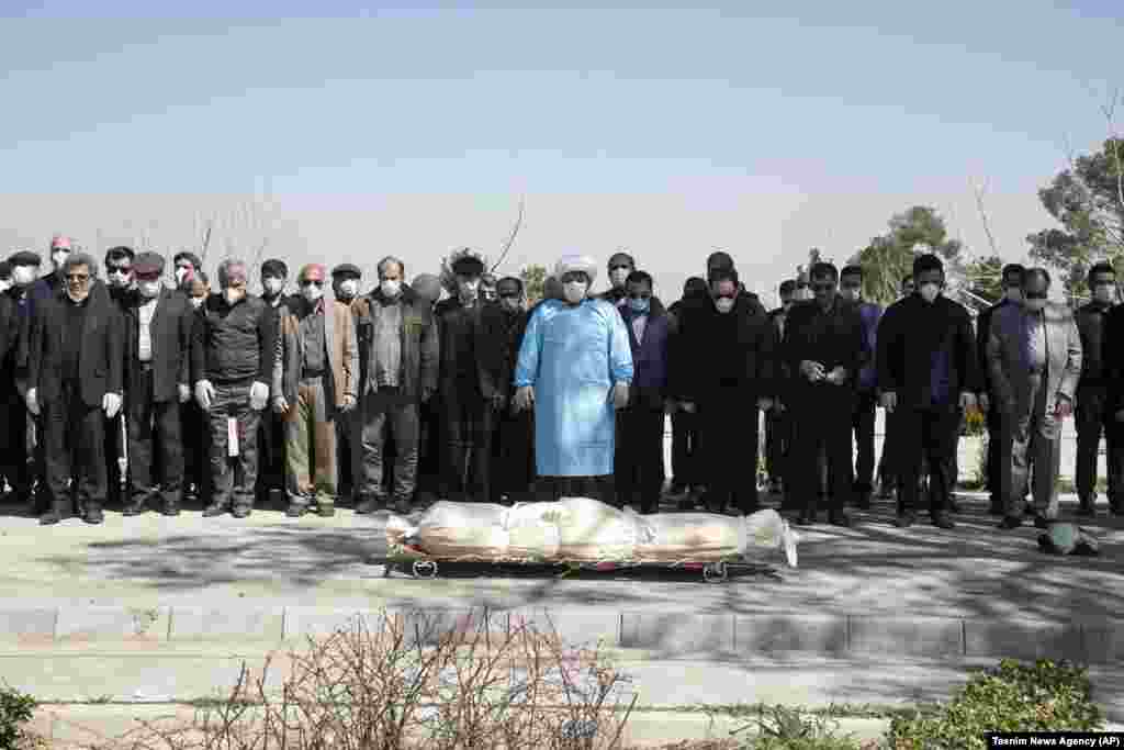 Mourners wearing face masks and gloves pray over the body of a former official in the Islamic Revolutionary Guards Corps, Farzad Tazari, who died March 9 after being infected with the new coronavirus, at the Behesht-e-Zahra cemetery just outside Tehran. (AP/Mahmood Hosseini/Tasnim News Agency)​