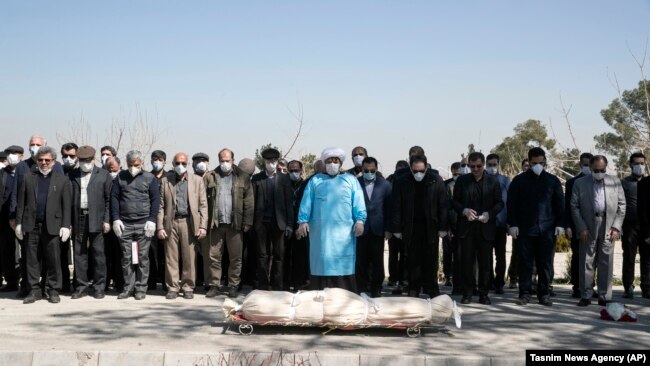 Mourners wearing face masks and gloves pray over the body of a former official in the Revolutionary Guard who died on March 9 after being infected with the new coronavirus, at the Behesht-e-Zahra cemetery just outside Tehran.