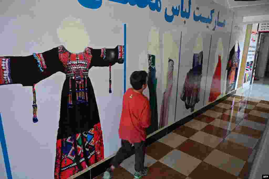 A boy walks through the corridor of a clothing market in which every female face of models has been painted over.