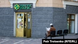 Мужчина читает газету рядом с отделением коммерческого банка в Алматы