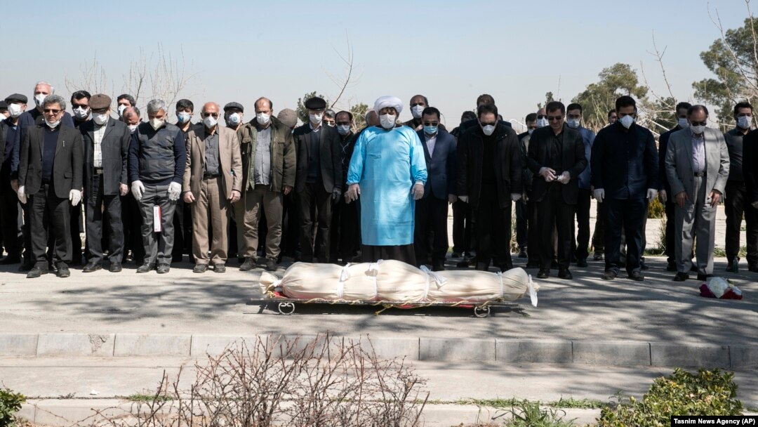 Mourners wearing face masks and gloves pray over the body of a former official in the Islamic Revolutionary Guards Corps, Farzad Tazari, who died on May 9 after being infected with the new coronavirus, at the Behesht-e-Zahra cemetery just outside Tehran on March 10.