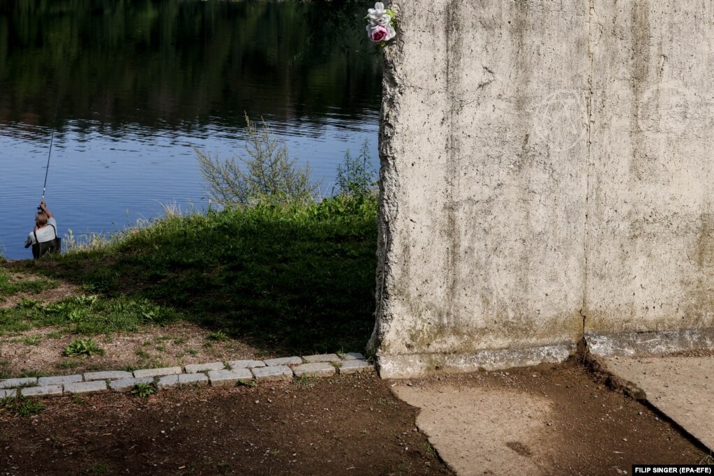 Një burrë duke peshkuar pranë një pjese të mbetur të Murit të Berlinit, me një lule të vendosur në skaj, në një vend përkujtimor afër Lumit Gribnic, në Berlin. (6 gusht)