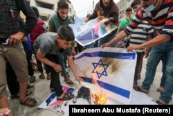 Palestinienii ard o reprezentare a unui steag israelian în timp ce un băiat pășește pe un afiș care îl înfățișează pe prim-ministrul israelian Benjamin Netanyahu în timpul unui protest anti-Israel asupra tensiunii din Ierusalim, în sudul Fâșiei Gaza, 24 aprilie 2021.