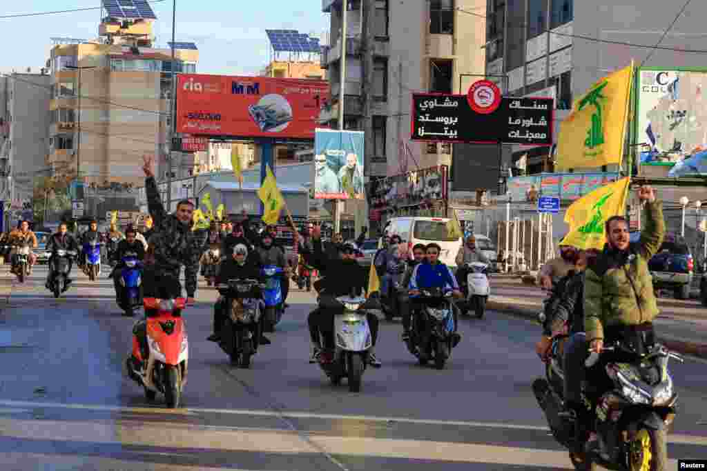 Disa burra mbajnë flamurin e Hezbollahut teksa kalojnë hipur mbi motoçikleta në hyrje të periferive jugore të Bejrutit pas nisjes së armëpushimit.