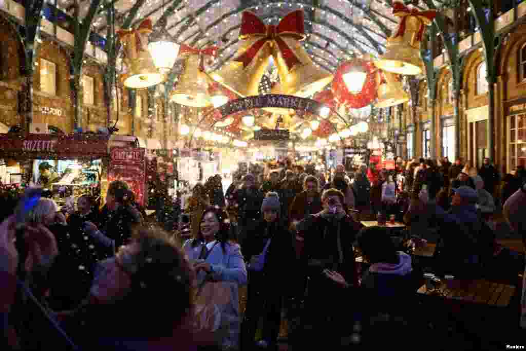 Oamenii se plimbă prin târgul de Crăciun din Covent Garden, Londra, în timp ce ninge artificial, pe 7 decembrie 2025.