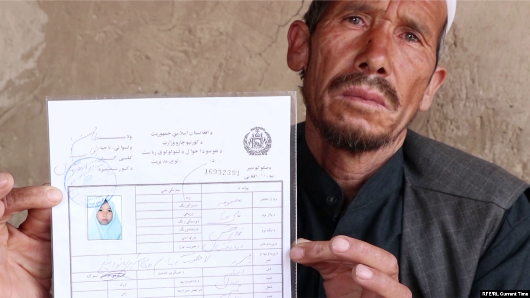 The father of a 15-year-old girl killed in the May 8 attack on Kabul's Sayed Al-Shuhada School holds his slain daughter's ID. "Masuma was both a son and a daughter for us," he said.
