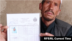 The father of a 15-year-old girl killed in the May 8 attack on Kabul's Sayed Al-Shuhada School holds his slain daughter's ID. "Masuma was both a son and a daughter for us," he said.