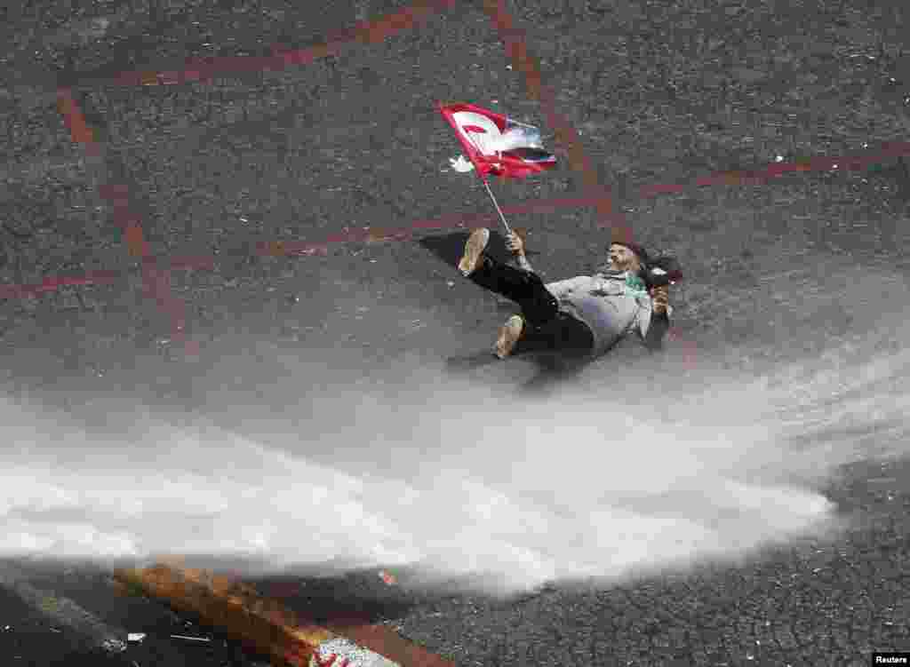 A protester holding a flag bearing an image of Mustafa Kemal Ataturk, founder of modern Turkey, falls as he is hit by a jet of water from a police water cannon during clashes on Istanbul&#39;s Taksim Square. (Reuters/Osman Orsal)