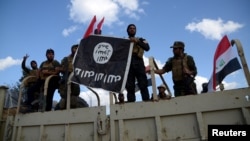 Shi'ite paramilitary fighters hold an Islamic State flag that they pulled down in Tikrit on March 31.