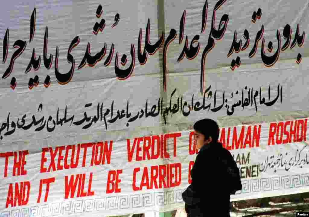 A boy stands in front of a banner reading &quot;The execution verdict of Salman Rushdi will be carried out&quot; at Tehran University in February 2012.