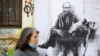 BULGARIA – A woman walks past a poster depicting Russian President Vladimir Putin holding his own body, as Russia's invasion of Ukraine continues, in Sofia, Bulgaria, March 28, 2022