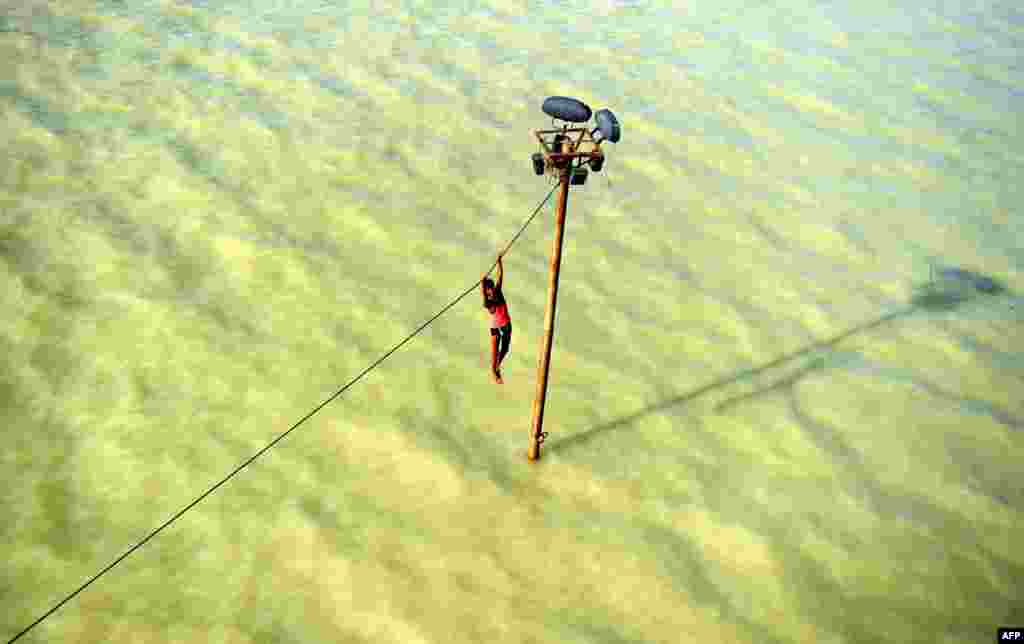 A youth dangles from a power line before diving into the floodwaters of an overflowing Ganges River in Allahabad, India. (AFP/Sanjay Kanojia)