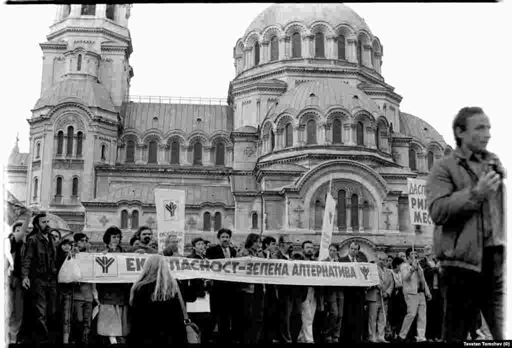 Шествието на &quot;Екогласност&quot; приближава задния вход на парламента. Зад транспаранта, отляво на дясно: Вера Младенова (киновед), Петър Стайков (психолог), неидентифициран участник, Никола Ковачев (режисьор), Димитрина Петрова (философ), Петър Берон (биолог), Петър Слабаков (актьор), Александър Каракачанов (философ), Цветан Кардашев (философ), Румен Данов (икономист), Делчо Вичев (инженер), Пирин Воденичаров (химик).