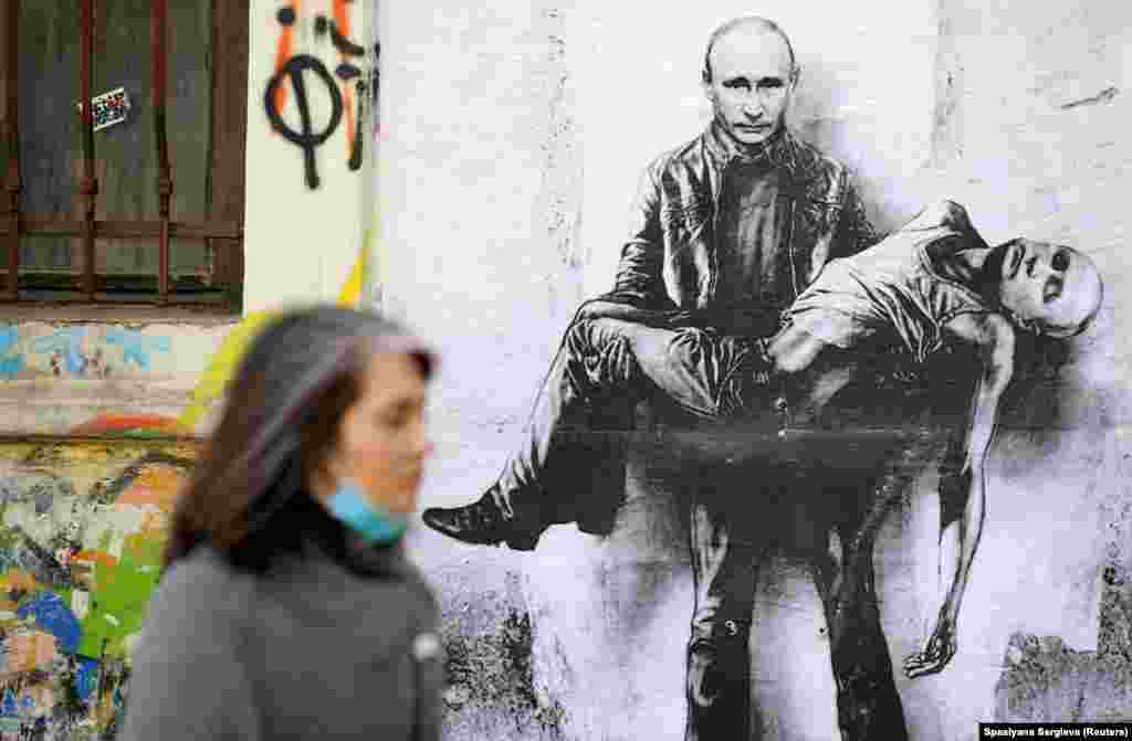 A woman walks past a poster depicting Russian President Vladimir Putin holding his own body, as Russia's invasion of Ukraine continues, in Sofia.