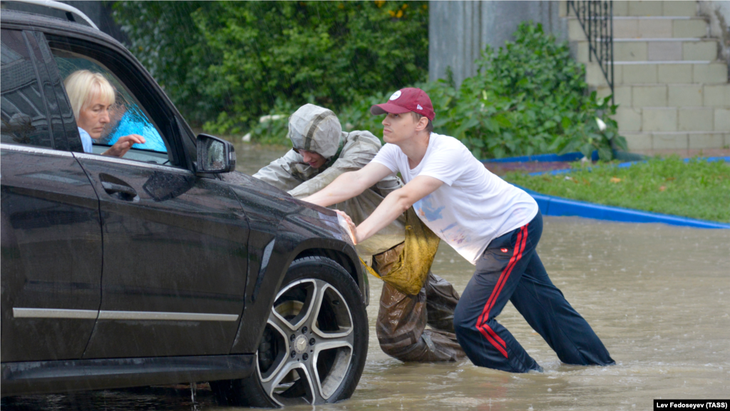 Чоловіки штовхають автомобіль на підтопленій вулиці. Російська влада Керчі рекомендує утриматися від поїздок на особистому автотранспорті