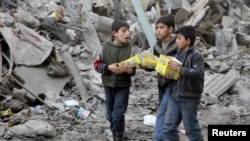 Boys carry boxes of biscuits near rubble of damaged buildings in Aleppo.