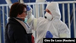 A person wearing a protective suit and mask checks the temperature of people departing from the ferry port of Molo Beverello after Italy orders a countrywide lockdown to try and contain a coronavirus outbreak, in Naples, Italy,