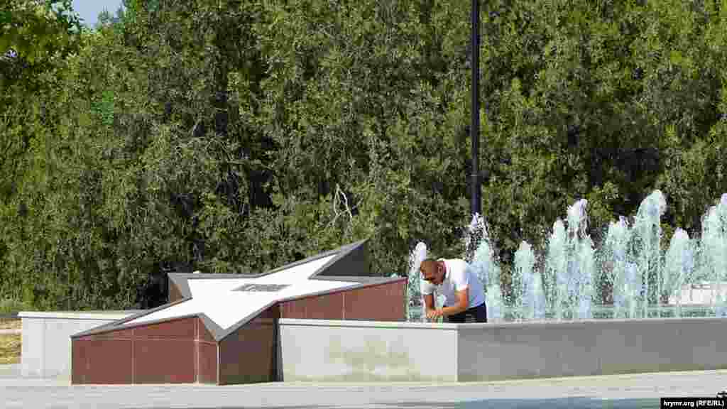 Посетитель парка спасается от жары в фонтане