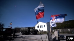 Прапор Росії, Сербії та ВМС Росії (на фото: 13 березня 2014 року), коли російська військова вантажівка проїжджає через блокпост на шляху з Сімферополя до Севастополя на Кримському півострові, який був анексований Росією в 2014 році