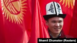 A man wearing the Kyrgyz national hat poses with national flags before a rally marking the Day of Flag and the Day of Kalpak in Bishkek in March 2013.