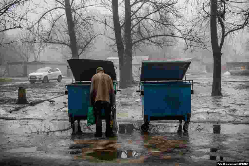 A man searches through a trash bin in a residential area.