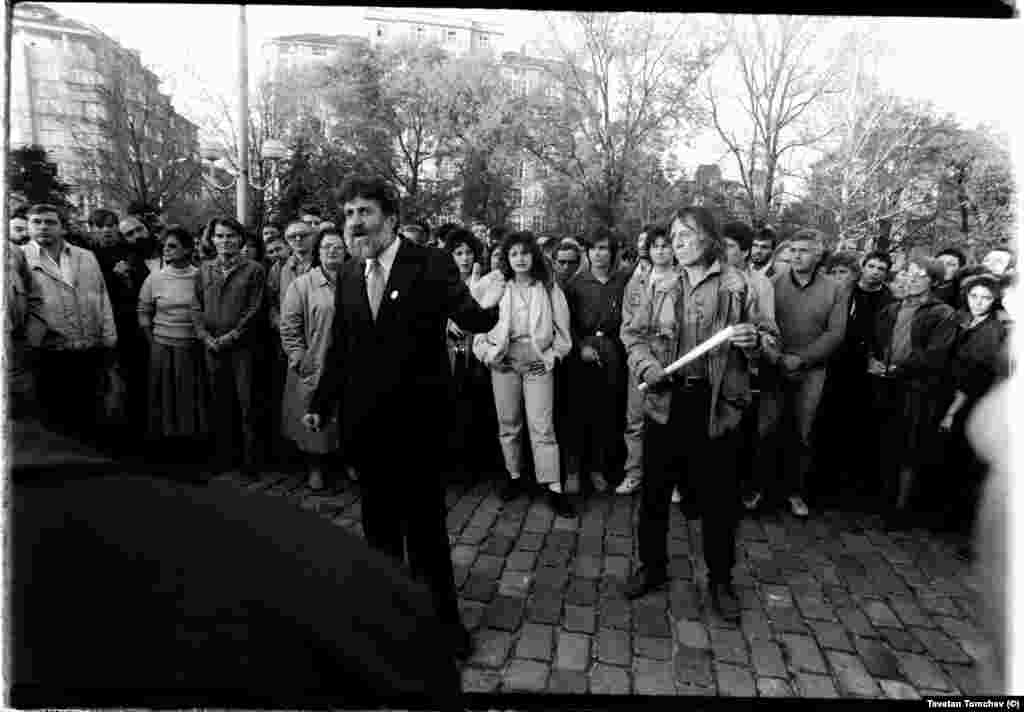 Петър Берон (в тъмен костъм, вляво) и Петър Слабаков говорят пред събралите се хора. И двамата са съучредители на &quot;Екогласност&quot; (1989), а по-късно депутати от СДС в Седмото Велико народно събрание (1990-1991) и съавтори на конституцията (1991). И двамата се разделят бързо със СДС, макар и по различни причини.