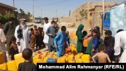 گروهی از کودکان و بزرگسالان در ولسوالی آقچۀ جوزجان در انتظار پُر کردن بشکه‌های آب.