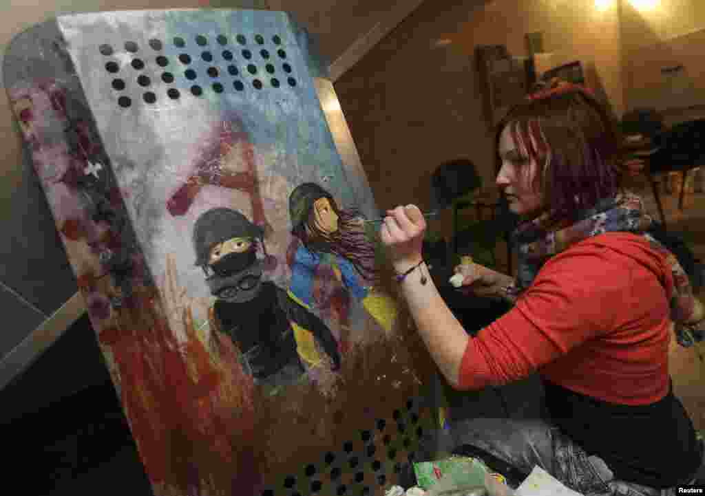 An artist decorates the shield of an antigovernment protester in Kyiv.