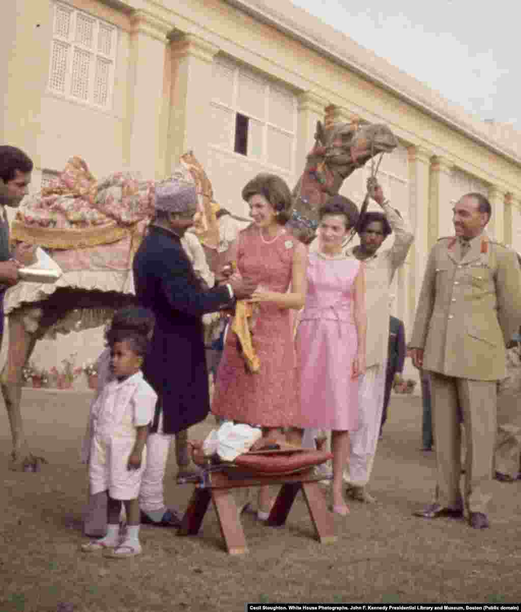 First lady Jacqueline Kennedy and her sister, Lee Radziwill, meet camel driver Bashir Ahmad. Ahmad had formed a friendship with U.S. Vice President Lyndon Johnson the year before after Johnson stopped to shake the camel driver&#39;s hand on his own trip to Pakistan. After Johnson casually invited Bashir to &quot;come see me sometime,&quot; Bashir accepted the invitation. He became a media spectacle after he traveled to the United States to meet with Johnson and the Kennedys.&nbsp;