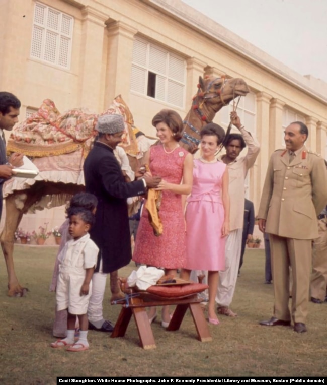 First lady Jacqueline Kennedy and her sister, Lee Radziwill, meet camel driver Bashir Ahmad. Ahmad had formed a friendship with U.S. Vice President Lyndon Johnson the year before after Johnson stopped to shake the camel driver's hand on his own trip to Pakistan. After Johnson casually invited Bashir to "come see me sometime," Bashir accepted the invitation. He became a media spectacle after he traveled to the United States to meet with Johnson and the Kennedys.