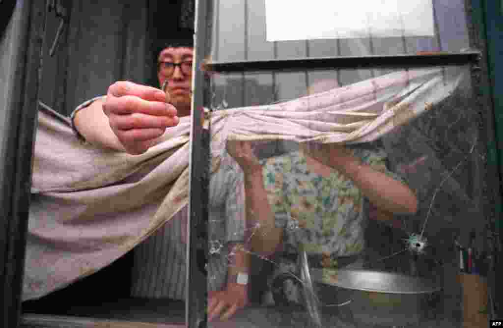 Stanovnik Pekinga pokazuje metak iz automatske puške koji je probio prozor njegvog stana.