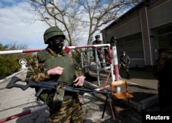 Українські військовослужбовці спостерігають за озброєним російським солдатом (на передньому плані), який блокує українську військову базу в Євпаторії 5 березня 2014 року