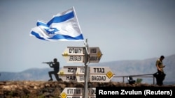 An Israeli soldier stands next to signs pointing out distances to different cities, on Mount Bental, an observation post in the Israeli-occupied Golan Heights that overlooks the Syrian side of the Quneitra crossing, May 10, 2018