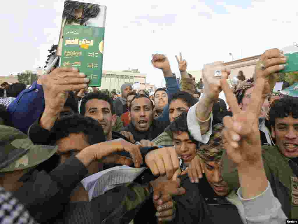 تظاهرکنندگان جلد نیمه سوخته «کتاب سبز» نوشته معمر قذافی را در دست گرفته اند