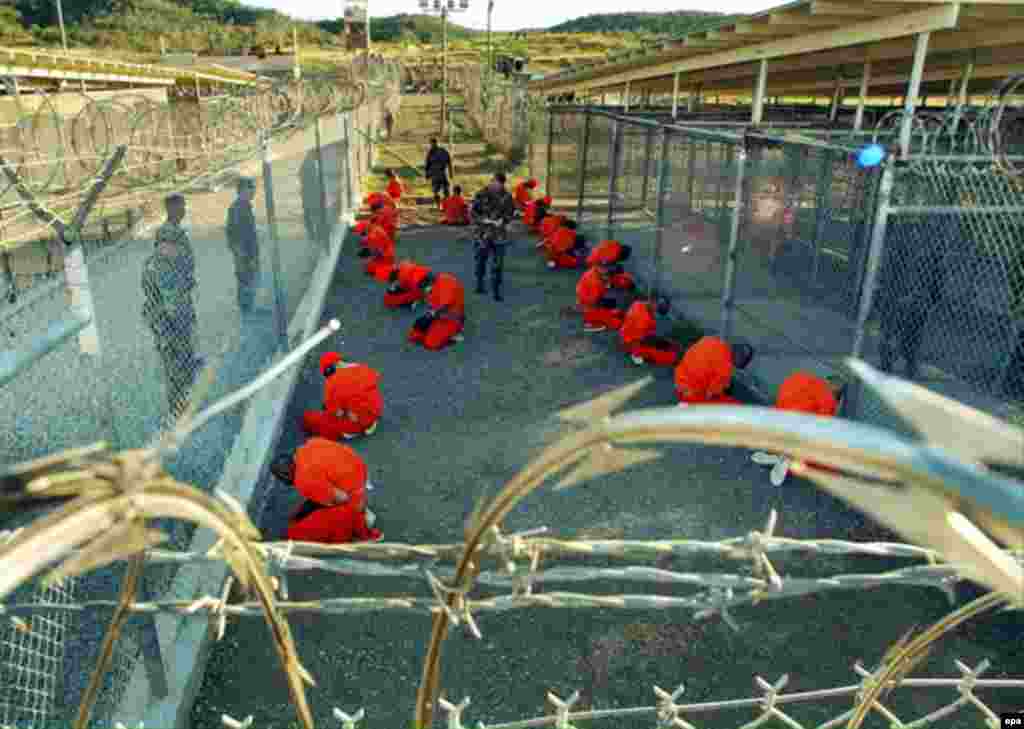 Detainees in orange jumpsuits sit in a holding area under the eyes of U.S. military police at Guantanamo Bay in this photograph, released in January 2002.