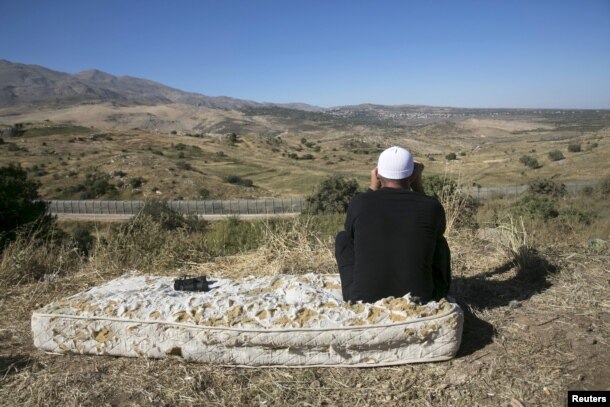Мужчина-друз сидит на старом матрасе у границы Израиля и Сирии, наблюдая в бинокль за боевым столкновением на сирийской стороне