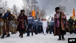 Surrounded by folks in traditional garb, torchbearer Akhmetova Svetlana (center) holds the torch aloft as the Olympic flame passes through the city of Irkutsk on the way to Sochi. 