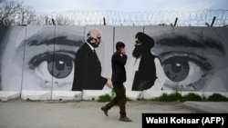 Чоловік у захисній масці від коронавірусу проходить повз стіну, на якій зображено рукостискання спеціального посланця США з питань Афганістану Залмая Халізада та одного з керівників «Талібану» 