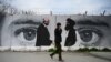 FILE: A man walks past a wall painted with images of U.S. Special Representative for Afghanistan Reconciliation Zalmay Khalilzad (L) and Taliban co-founder Mullah Abdul Ghani Baradar.