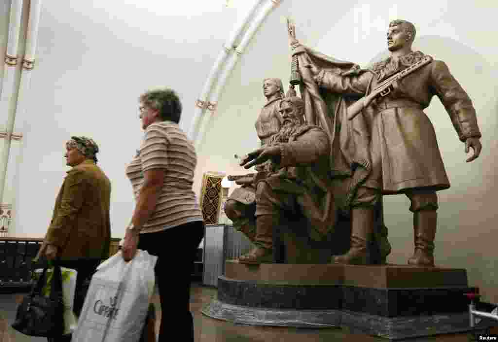 Women walk past a statue at the Belorusskaya metro station.