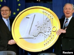 Fostul comisar european pentru afaceri monetare, Yves-Thibault de Silguy (stânga) și fostul președinte al Comisiei Europene, Jacques Santer, țin în mână un model de monedă euro, 1 mai 1998.