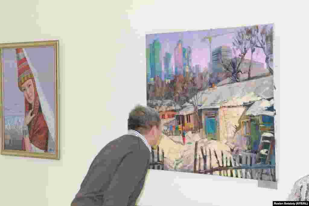 Посетитель смотрит на картину, где изображена молодая женщина, развешивающая белье во дворе дома.