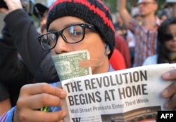 Жұмыссыздыққа наразы демонстрант "Революцияны әуелі өз үйіңде жаса" деген плакат көтеріп тұр. Нью-Йорк, 5 қазан 2011 жыл