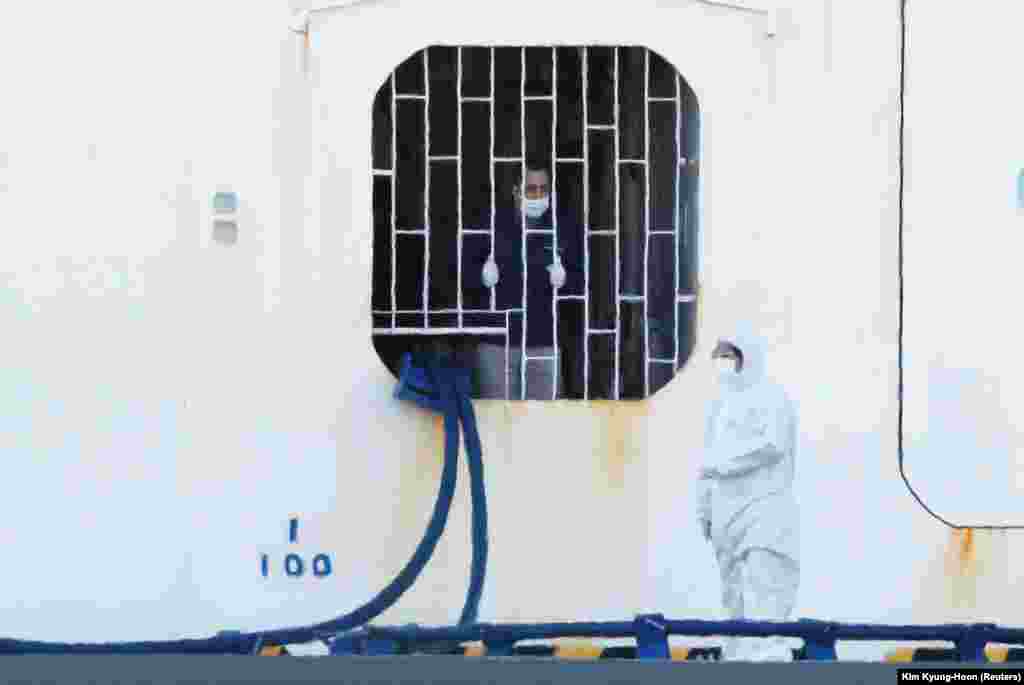 A crew member of the Diamond Princess talks to a worker in protective gear.&nbsp;Crew and passengers are now required to wear gloves and a face mask at all times when outside their cabins. &nbsp;