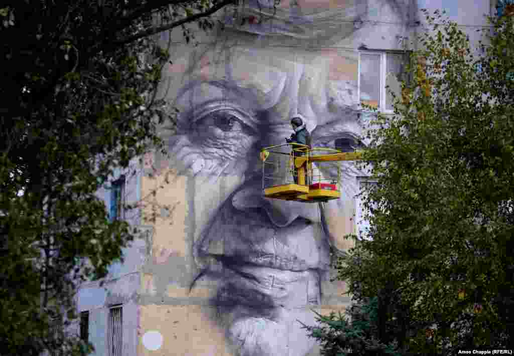 Wearing a flak jacket and ballistic helmet, Guido van Helten nears completion of his portrait of a local woman.&nbsp;