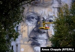 Wearing a flak jacket and ballistic helmet, Guido van Helten nears completion of his portrait of a local woman in Avdiyivka, eastern Ukraine.