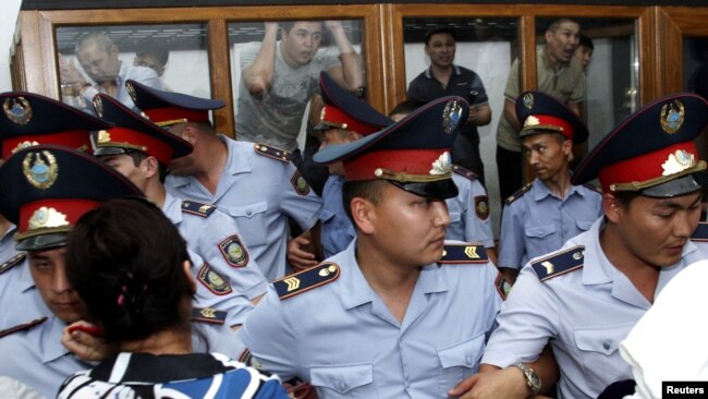 Сотрудники полиции перед помещенными в огороженную стеклом кабину фигурантами «Жанаозенского дела». Актау, 4 июня 2012 года.
