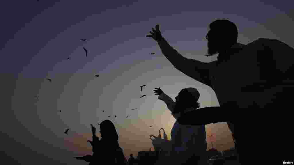 People are silhouetted against the sun while feeding birds in Karachi, Pakistan on December 30. (Reuters/Athar Hussain)